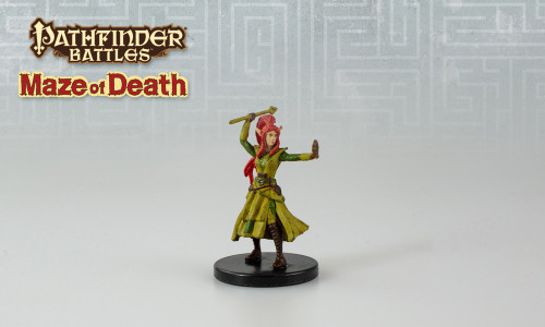 An image of a redheaded elf mystic in mismatched green robes and tall dark boots. Over her head she holds a javelin ready to throw. (Front View)