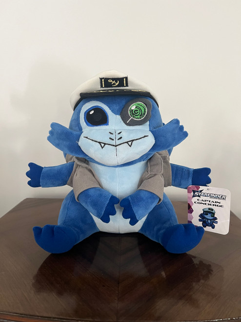 Captain Concierge Plushie. Photograph of a sweet-faced, six-armed alien in a pilot’s hat. It has a cybernetic eye.
