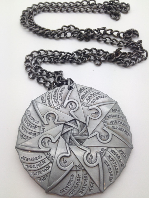 Sihedron Medallion shows the back side of a circular metal medallion with an attached chain. The medallion’s face is decorated with a seven-pointed star.