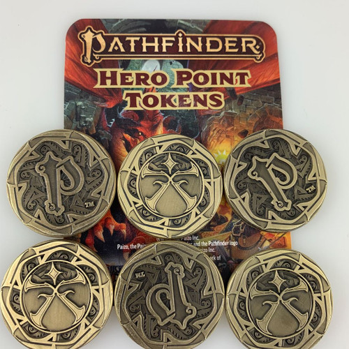 Pathfinder Hero Point Tokens (Pack of 6) shows a six brass-colored coins sitting atop a cardboard label featuring the Pathfinder Hero Point Tokens logo and an image of heroes fighting a dragon, but the image is mostly covered by the six coins; three coins show a stylized capital letter P, while the other three show a vaguely “X” shaped spiky symbol under a four-pointed star.