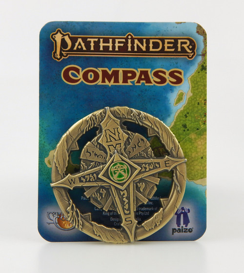 Pathfinder Compass shows a cardboard card illustrated with a partial map of a green coastline and blue ocean on which is mounted a brass-colored compass featuring a four-pointed compass rose, at the middle of which is a green and gold symbol.