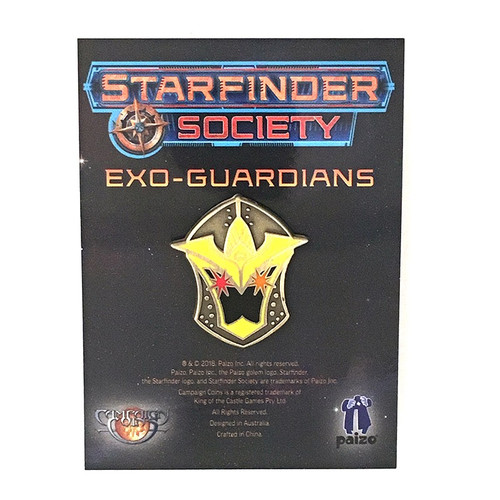 Starfinder Society Faction Pin: Exo-Guardians shows a black cardboard card on which is affixed a helmet-shaped pin in front of a dark yellow background; the gold helmet has a spiky top and two stars (one red and one orange) inside where ones eyes would peer out of, all above a few lines of descriptive text on the cardboard below.