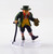 This small humanoid has pointed ears, green eyes, and a wicked grin. He carries a small pouch in one hand and a walking stick in the other. He has flaming red hair and muttonchops beneath a buckled green hat that matches his green suit. Striped socks stick out from buckled shoes. (Front View)