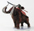 This huge elephantine creature is covered in a thick, shaggy coat of brown fur. It lets out a territorial trumpet from its long trunk, curling upward between two long, curved tusks. Red war paint marks its body beneath a large, red saddle blanket on top of which sits its rider, a screaming orc in war dress carrying a crude naginata. (Side View)