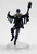 Beneath ragged shreds, this lean figure’s chalky skin darkens to charred hues at the extremities. This dancer is mid leap, one knee high up in the air. In its left hand is a decorative scepter topped with a humanoid skull. (Front View)