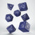 7 cobalt blue polyhedral dice of different shapes suspended in air. Each die has silver decorative designs on each side, along with a number.