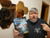 Starfinder: THE GAP photo shows a puzzled bearded man holding the book in front of several hexagonal mirrors on the wall behind him as he points at the book in his other hand; the book cover shows a swirling churn of mist and stars and planets and darkness.