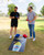 Two men standing over the black cornhole boards with the yellow shaved ice graphic, playing a game with blue and red bean bags.