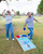 A man and woman celebrating enthusiastically while playing cornhole on the teal boards with the 'FLAVOR YOUR LIFE' graphic.