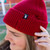 Close-up of a person wearing the maroon beanie, showing the small tag with the colorful shaved ice cup icon.
