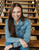 Smiling woman sitting on stairs, wearing the light wash denim jacket with the shaved ice cup icon.
