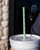A light mint green reusable straw with a small fruit pattern, inserted in the lid of a cup.