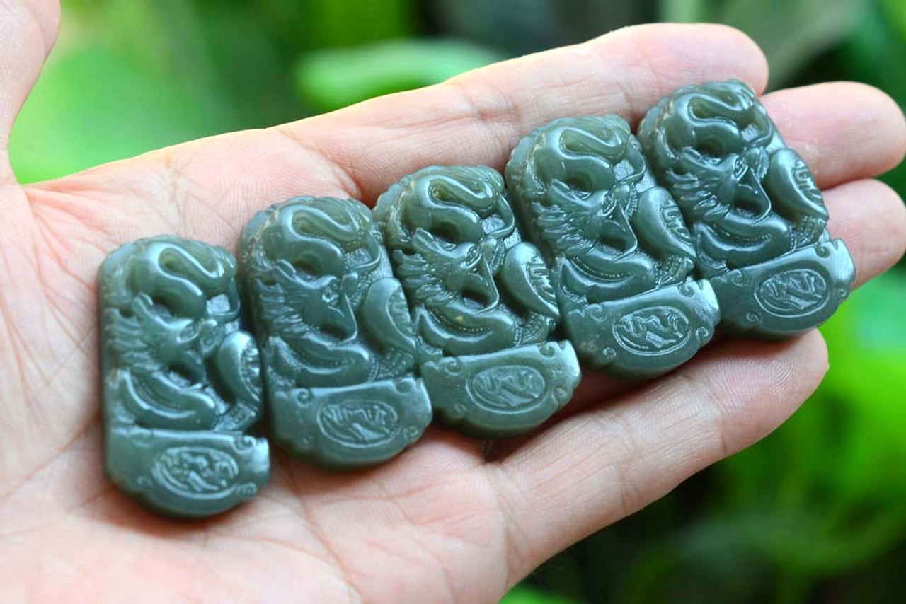 Item 2 - Group of darker-tone dragon pendants in hand under natural light