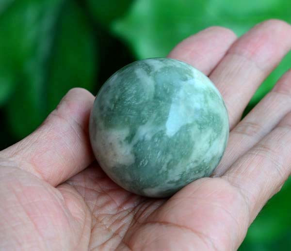 Single Jianghua Xiuyan jade sphere in hand under natural light, cloudy texture visible