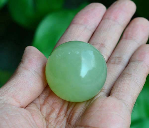 Single Xiuyan jade sphere in hand, soft green translucent color