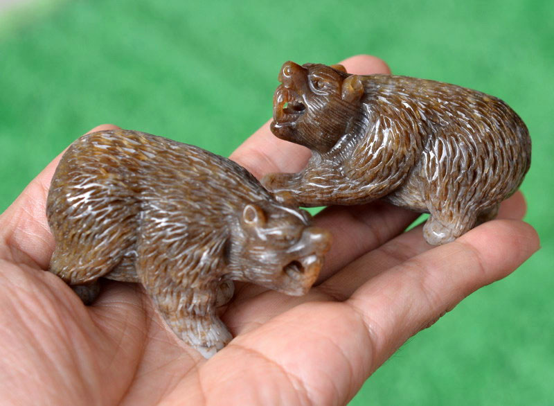 Pair of hand-carved brown nephrite jade bear figurines shown in hand under natural light
