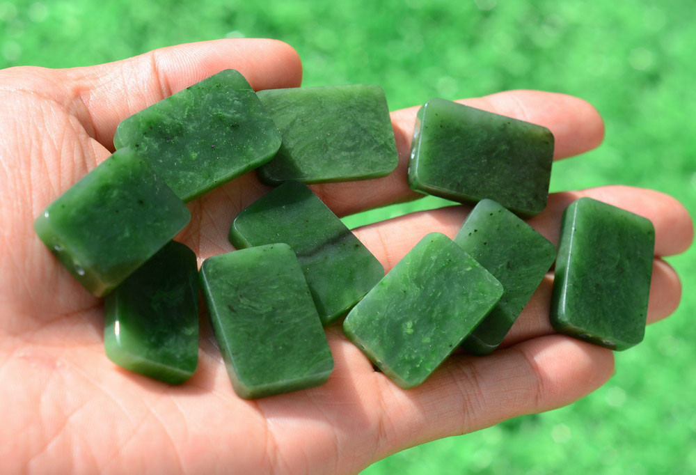G026541A Hand holding a cluster of Variant A genuine nephrite jade carving blanks in natural sunlight.