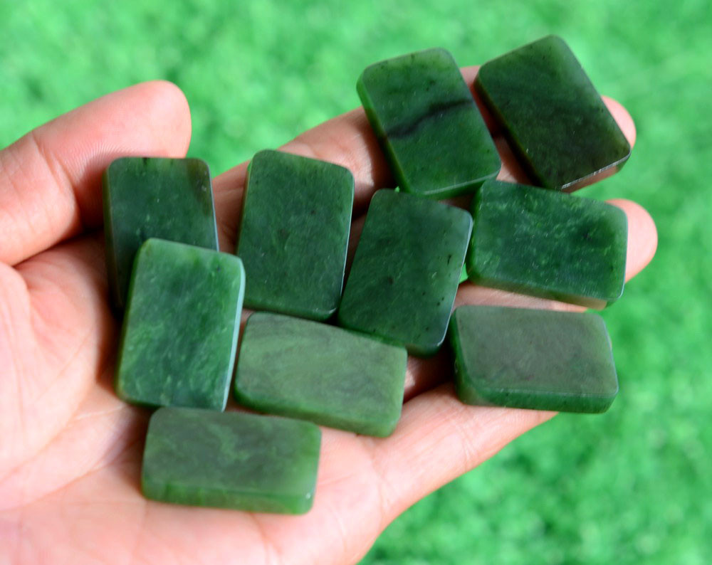 G026541A Multiple Variant A uncarved Canadian jade plaques with visible mineral inclusions held outdoors.