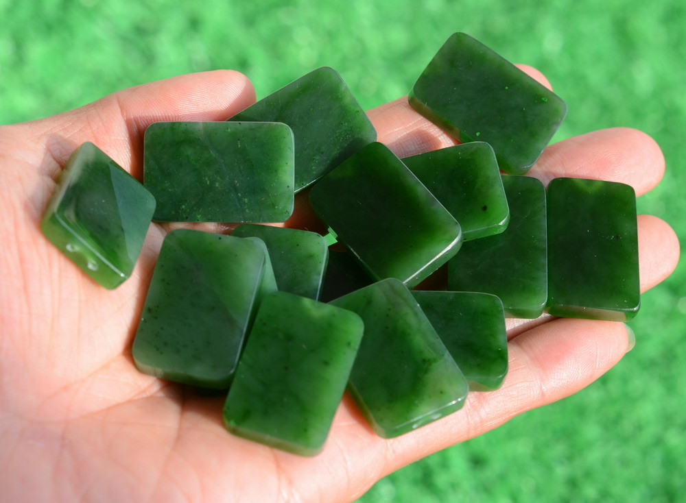 G026541B Hand holding Variant B premium green jade peace plaques in sunlight showing smooth texture.