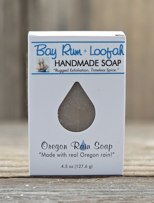 4.5 oz Bay Rum & Loofah Soap in a box with a raindrop cutout showing the exfoliating bar, displayed on a wooden surface.
