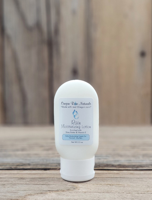 2.5 oz bottle of Rain Moisturizing Lotion on a wooden surface, featuring rain‑inspired imagery on the label.