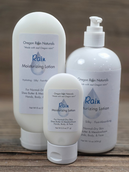 Rain Moisturizing Lotion in three sizes—2.5 oz, 8 oz, and 16 oz bottles displayed on a wooden background.