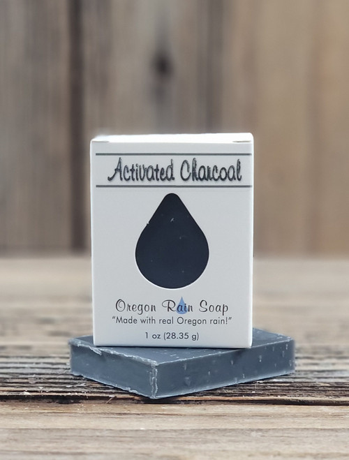 1 oz Activated Charcoal Pure Essence Soap bar with a raindrop cutout showing the dark black activated charcoal bar, displayed on a wooden surface.