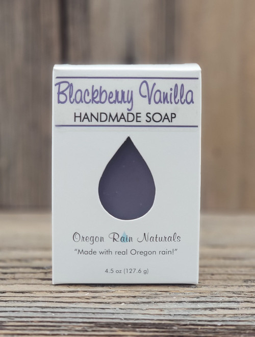 4.5 oz Blackberry Vanilla Handmade Soap in a white box with a purple raindrop cutout showing the berry‑colored bar, displayed on a wooden surface.