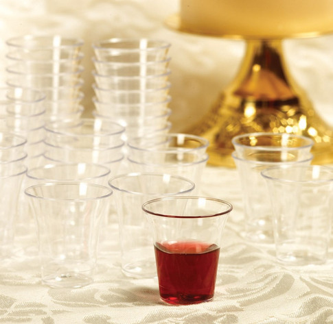 Clear plastic communion cups arranged on church table with one cup filled with red grape juice