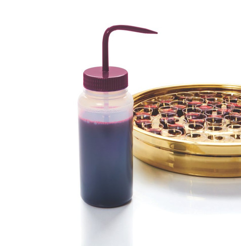 Communion cup filler bottle filled with grape juice beside gold communion tray