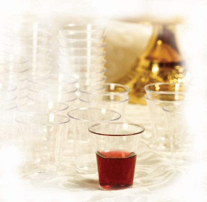 Clear plastic communion cups arranged on church table with one cup filled with red grape juice