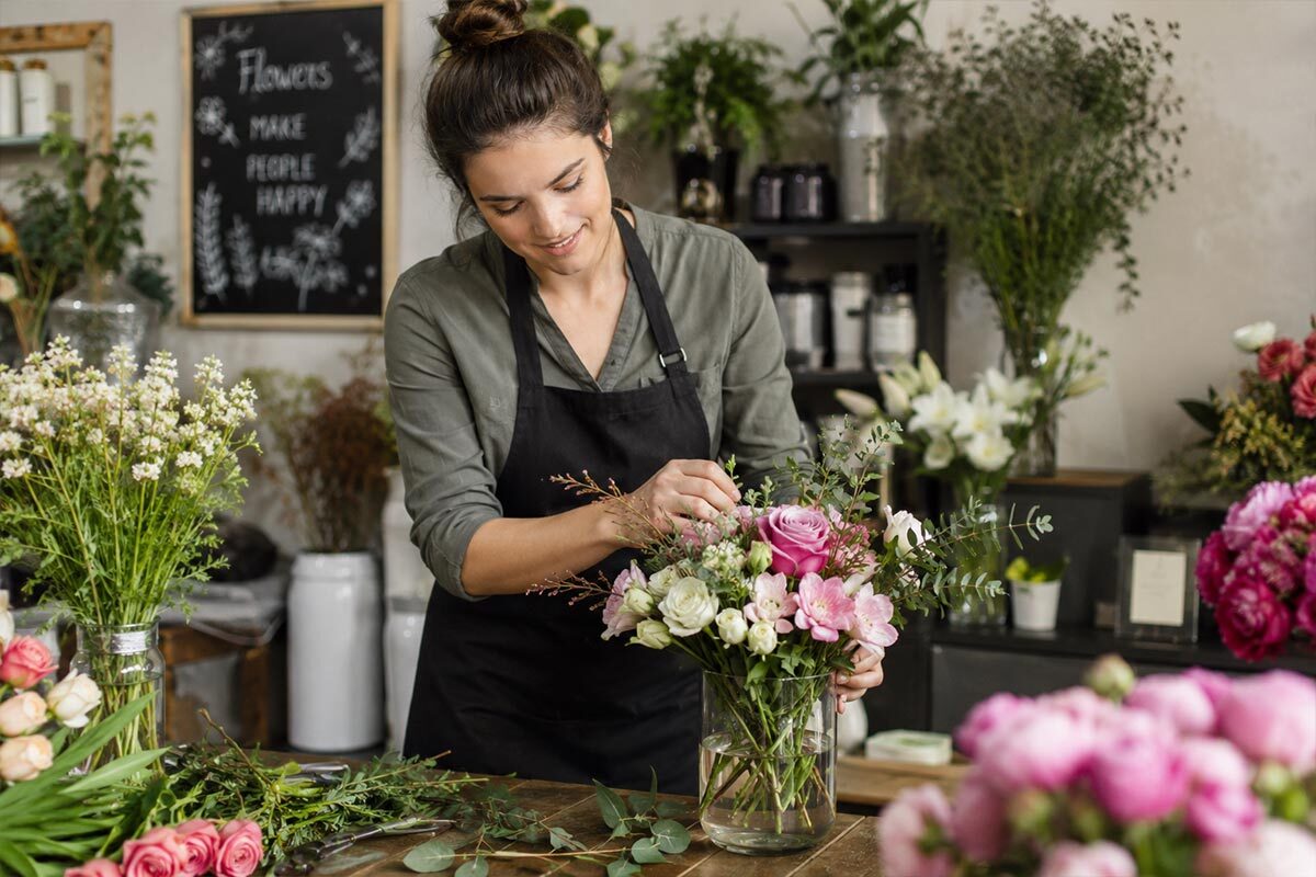 Florist arranging a pink floral bouquet inside a cozy flower shop.