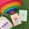 Rainbow stacking toy, colorful wooden arcs arranged from red to purple on green grass, with emotion flashcards and a canvas bag for emotional learning.