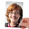 Photo print of a smiling child, young boy with red hair and glasses, holding the photo with his face on it.