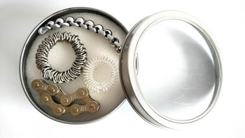 Product Kit, contains metal chain, metal spring, metal brush, and a small metal chain link inside a round metallic container.