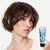 Reuzel Grooming Cream 100ml, image of a woman with short brunette hair and clear skin holding a tube of Reuzel Grooming Cream with a blue and silver label.