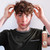 Reuzel Surf Tonic 100ml, a man with curly hair adjusting his hairstyle, holding the product bottle in the foreground.