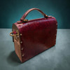Side and back profile of the structured leather handbag displaying brass studs and patterned side gussets.