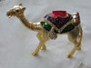 A detailed close-up highlighting the intricate red and blue stones, gold finish, and ornate saddle design of the camel figurine.