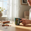 A steaming ceramic coffee mug featuring a deep teal background adorned with vibrant orange, pink, and purple traditional Persian floral patterns.