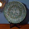 A stunning 30 cm handmade clay plate featuring white Islamic calligraphy over a vibrant teal-green floral pointillist background.