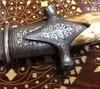 Close-up of the smooth camel bone hilt and the detailed metalwork at the base of the decorative Arabic blade.