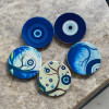 A top-down view of five circular ceramic coasters arranged together, highlighting the varied blue-toned Evil Eye motifs.