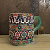 A professional product shot of the hand-painted embossed ceramic mug styled neatly against a rustic backdrop.
