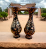 Product photo of the 16 cm copper engraved birds and flowers pattern vase set, showcasing a matching pair of bulbous teardrop-shaped vessels with flared necks, coated in a rich midnight black enamel that is meticulously etched away to reveal gleaming rose-gold copper flying birds and blooming blossom branches, standing on a light-colored wooden table structure against a white paneled wall background.