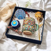An overhead view of the birth flower gift box containing a hand-painted floral clay mug, a gold rose, and a blue ceramic evil eye.