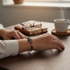 A lifestyle close-up showing the intricate, hand-painted enamel details of the Minakari bracelet on a wrist against a warm, sunlit office background.