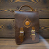 The front of the Nomad Executive Vertical Satchel in dark brown cow leather with a sunburst stitched emblem.