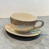 A professional product shot of the elegant hand-painted ceramic tea cup and matching saucer resting on a neutral gray backdrop.
