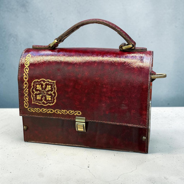 A deep red genuine cow leather structured handbag featuring an ornate gold scroll pattern and a secure clasp on a neutral surface.
